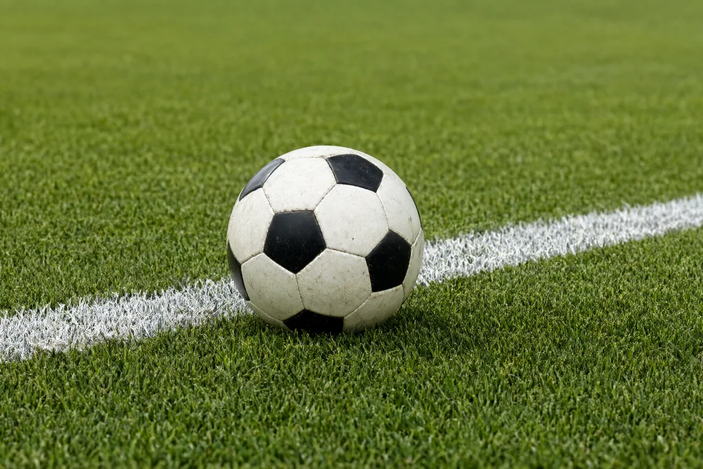 Marcações brancas de linha de baliza em relva cortada com uma bola parada sobre a linha